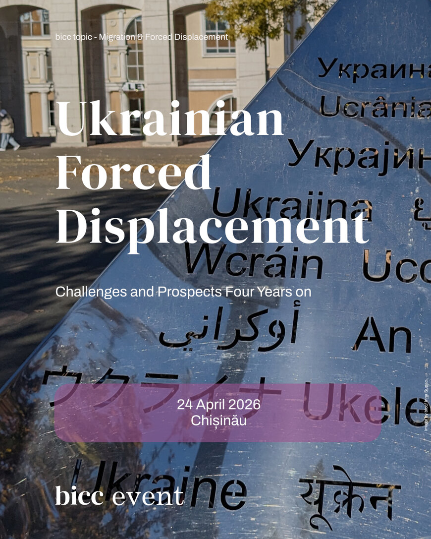 Metal sculpture with the word 'Ukraine' in multiple languages in an outdoor urban setting with buildings and trees in the background